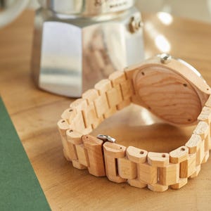 May include: A light wood wristwatch with a brown wood band. The watch is lying on a wooden surface.