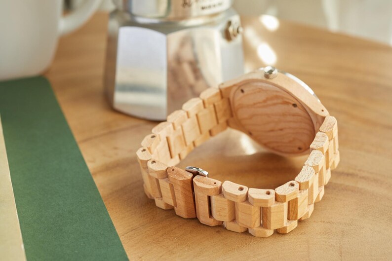 May include: A light wood wristwatch with a brown wood band. The watch is lying on a wooden surface.