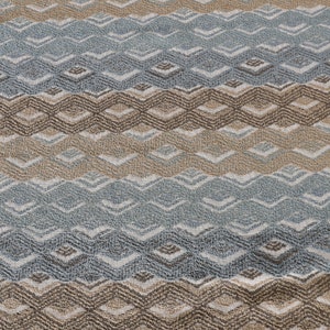 May include: A close-up of a woven fabric with a geometric pattern in shades of brown, beige, and blue. The fabric has a textured surface and a repeating pattern of diamonds and waves.
