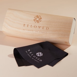 May include: A wooden box with the words "BELOVED" and the phrase "BE LOVED, BE LOVELY" engraved on the top. A black microfiber cleaning cloth with the same logo is next to the box.