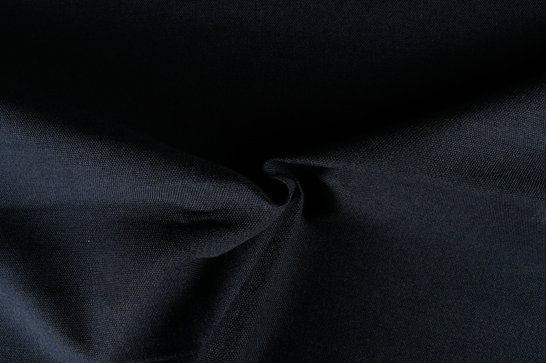 May include: Close-up of a dark blue fabric with a smooth, textured surface. The fabric is folded and draped, creating soft folds and shadows.