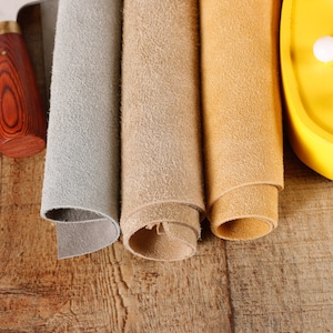 May include: Three rolls of leather in gray, beige, and brown, with a leather working tool.