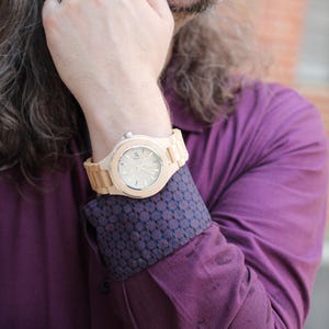 May include: A man wearing a purple shirt with a patterned cuff and a wooden wristwatch with a light brown band.