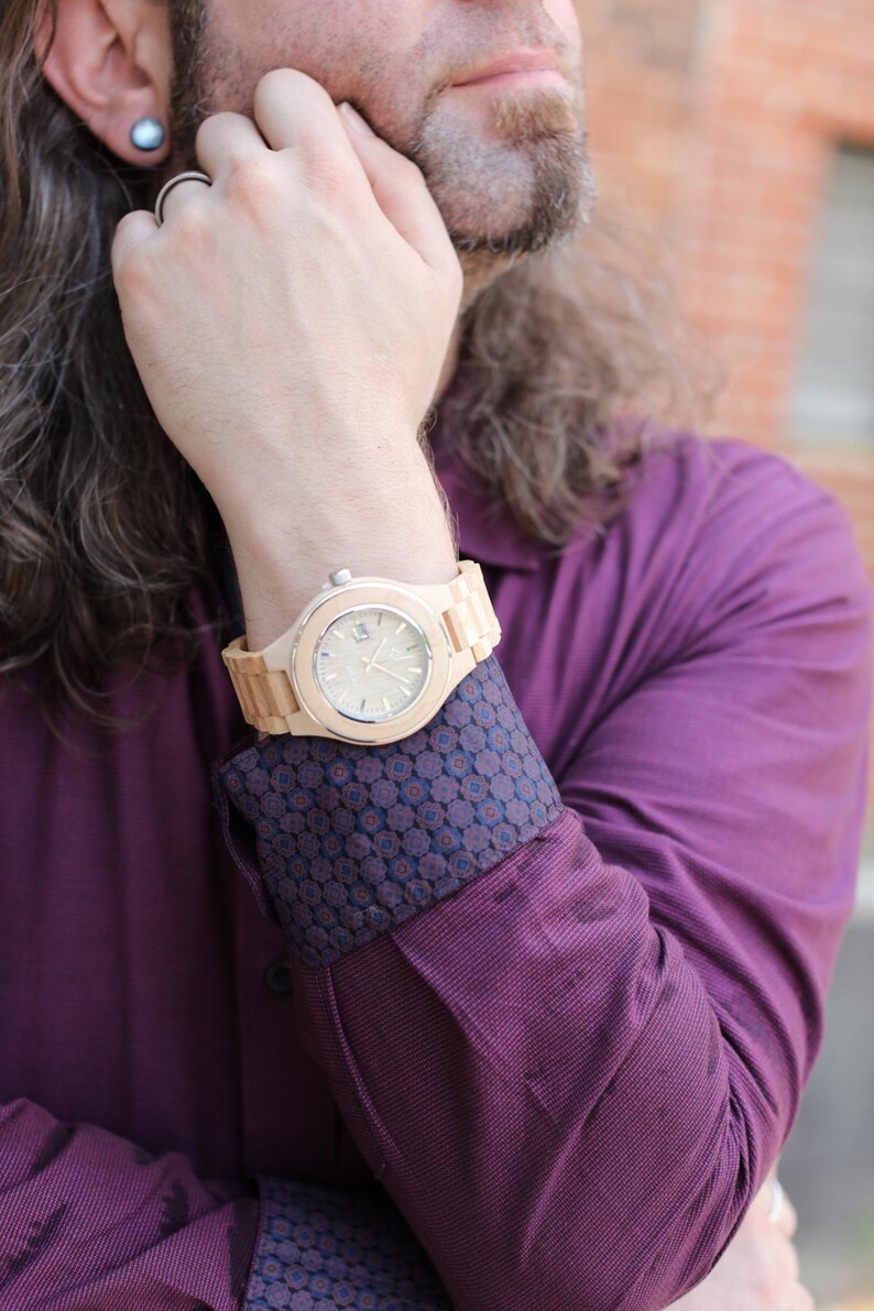 May include: A man wearing a purple shirt with a patterned cuff and a wooden wristwatch with a light brown band.