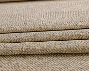 May include: Close-up of a beige fabric with a herringbone weave pattern. The fabric is folded in several layers, showing the texture and detail of the weave.