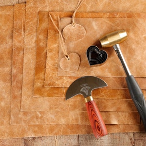 May include: A set of leather crafting tools including a leather mallet, a leather cutting tool, a heart-shaped leather punch, and several pieces of brown leather.