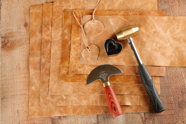 May include: A set of leather crafting tools including a leather mallet, a leather cutting tool, a heart-shaped leather punch, and several pieces of brown leather.
