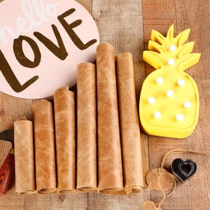 May include: Six rolls of brown leather, a small knife, a heart-shaped leather punch, two leather tags, and a yellow pineapple-shaped night light on a wooden surface. The sign says "hello LOVE".