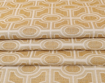 May include: Folded fabric with a repeating geometric pattern in gold and cream. The design features interlocking ovals and rectangular shapes, creating a textured surface. The fabric appears to be a woven material, suitable for upholstery.