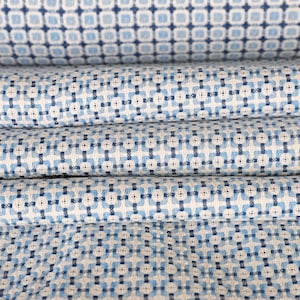 May include: Close-up of folded fabric with a repeating pattern of blue and white squares and cross-like shapes. The fabric is layered, showing the texture and design. The pattern is consistent across the material.