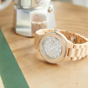 May include: A light wood wristwatch with a silver face and a light wood band.