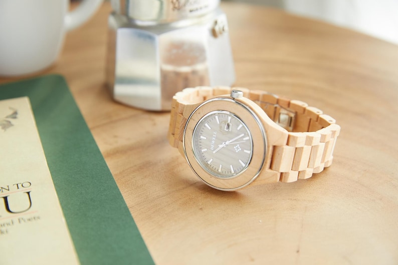 May include: A light wood wristwatch with a silver face and a light wood band.
