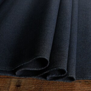 May include: Close-up of a dark blue fabric with a textured surface. The fabric is folded in thirds and the edges are sewn.