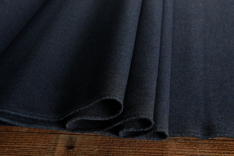 May include: Close-up of a dark blue fabric with a textured surface. The fabric is folded in thirds and the edges are sewn.