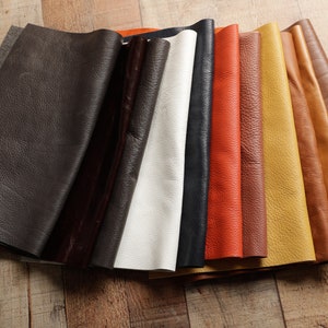 May include: A variety of leather swatches in different colors, including brown, black, white, orange, yellow, and tan. The leather is folded and arranged in a row.