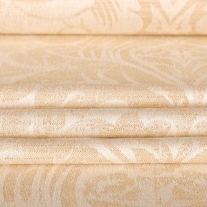 May include: Close-up of folded fabric with a repeating floral pattern in cream and off-white. The fabric is layered, showing the texture and design details. The folds create shadows, highlighting the pattern.