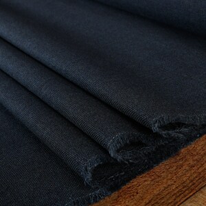May include: Close-up of a dark blue fabric with a textured weave. The fabric is folded and has a raw edge.