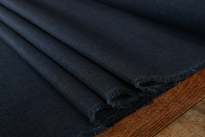 May include: Close-up of a dark blue fabric with a textured weave. The fabric is folded and has a raw edge.