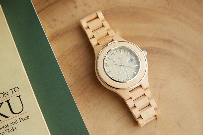 May include: A wooden wristwatch with a light brown band and a white face. The watch face has black hour and minute hands and a small black second hand.