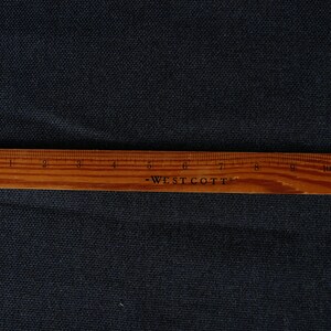 May include: A close-up of a dark blue fabric with a wooden ruler labeled "Westcott" measuring 12 inches.