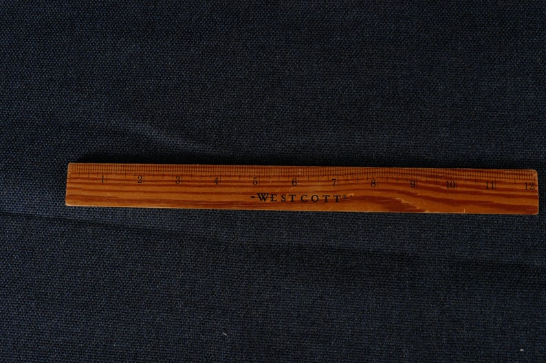 May include: A close-up of a dark blue fabric with a wooden ruler labeled "Westcott" measuring 12 inches.