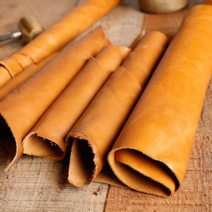 May include: Several rolls of light brown leather are stacked on top of each other on a wooden surface.