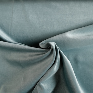 May include: A close-up of a soft, smooth, light blue fabric with a subtle sheen. The fabric is draped and folded, creating a textured background.
