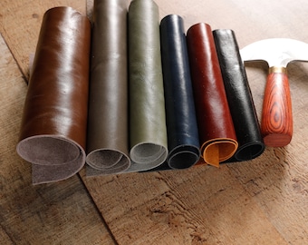May include: Assortment of rolled leather hides in various colors, including brown, gray, green, blue, red, and black, with a leather working tool.