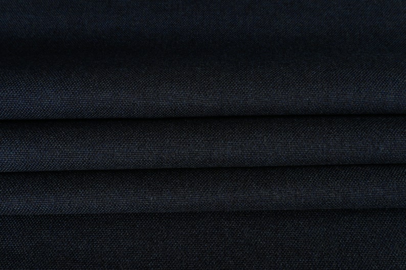 May include: Close-up of a dark blue fabric with a textured weave. The fabric is folded in several layers, showing the depth of the color and the subtle texture.