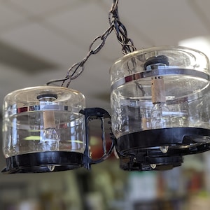 May include: A two-light glass pendant light fixture with black metal accents and clear glass shades. The light fixture is hanging from a chain.