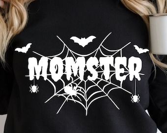 Könnte beinhalten: Schwarzes Sweatshirt mit weißem "MOMSTER"-Grafik, mit Spinnennetz, Fledermäusen und Spinnen. Das Design hat ein Halloween-Thema. Das Bild enthält auch den Text "SVG - PNG - EPS - DXF" und ein Logo für "Print Cuts SVG".