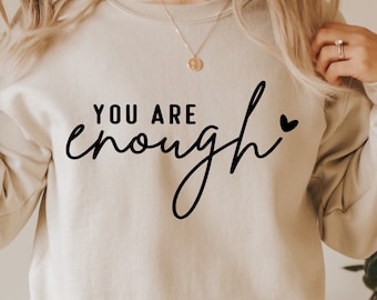 Peut inclure: Un sweat-shirt beige avec le texte "YOU ARE enough" en écriture noire avec un petit cœur.