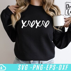 May include: A black sweatshirt with the text "XOXO" in white lettering. The sweatshirt is being worn by a person holding a white mug.