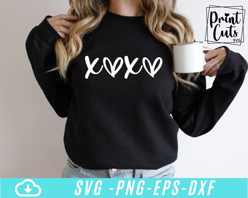 May include: A black sweatshirt with the text "XOXO" in white lettering. The sweatshirt is being worn by a person holding a white mug.