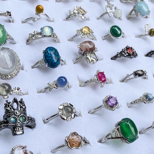 Peut inclure: Une collection de bagues assorties présentant diverses pierres précieuses et montures en métal, incluant des formes ovales, rondes et florales. Les bagues sont disposées en grille, montrant des couleurs variées comme le bleu, le vert, le rouge et le transparent.