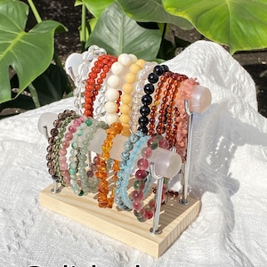 K&ouml;nnte beinhalten: Verschiedene Armb&auml;nder aus Edelsteinen in Rot, Wei&szlig;, Gelb, Schwarz und Rosa. Die Armb&auml;nder sind auf einem Holzst&auml;nder mit Metallst&uuml;tzen angeordnet. Das Wort "Polished" ist am unteren Bildrand zu sehen.