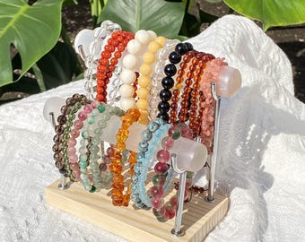 Puede incluir: Exhibición de pulseras de piedras preciosas en tonos rojos, blancos, amarillos, negros y rosas. Las pulseras están dispuestas sobre un soporte de madera con soportes metálicos. La palabra "Polished" está en la parte inferior de la imagen.