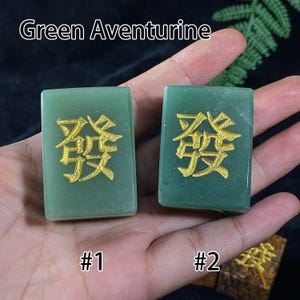 Pu&ograve; includere: Due pietre di avventurina verde con caratteri cinesi color oro. Le pietre sono rettangolari ed etichettate #1 e #2. Il testo "Green Aventurine" &egrave; nella parte superiore dell'immagine.