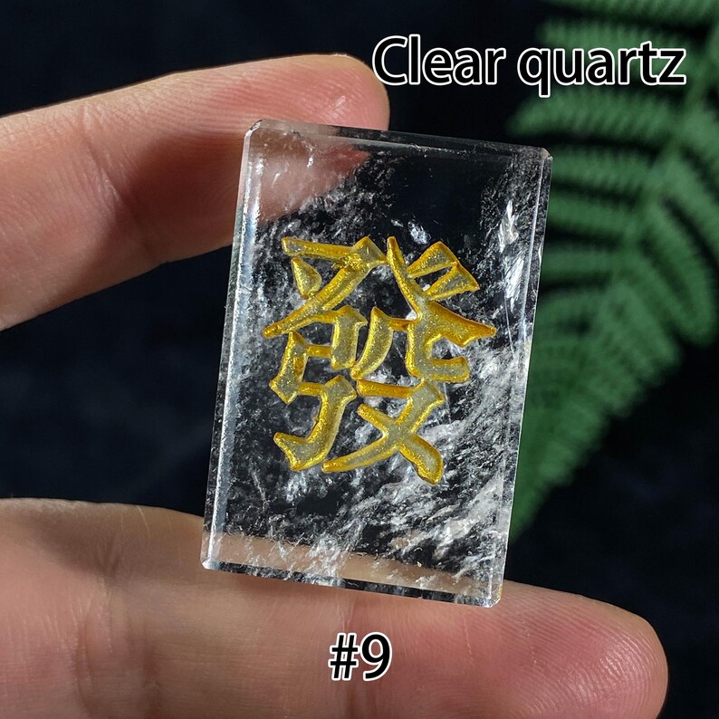 Pu&ograve; includere: Un rettangolo di cristallo di quarzo trasparente con caratteri cinesi dorati. Il testo "Clear quartz" &egrave; in alto e "#9" in basso. Il cristallo &egrave; tenuto dalle dita di una persona.