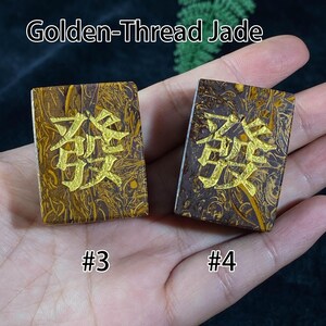 Pu&ograve; includere: Due pietre rettangolari di Giada Golden-Thread con caratteri cinesi dorati. Le pietre sono marroni con venature dorate e il testo "Golden-Thread Jade" &egrave; in alto. Le pietre sono etichettate #3 e #4.