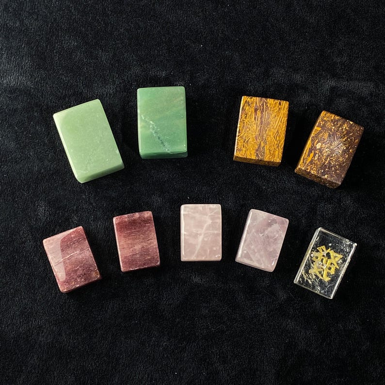 Pu&ograve; includere: Assortimento di pietre preziose rettangolari in vari colori, tra cui verde, marrone, rosa e trasparente. Le pietre sono disposte su una superficie nera, mostrando le loro trame e tonalit&agrave; uniche. Le pietre preziose sono probabilmente utilizzate per scopi decorativi o spirituali.