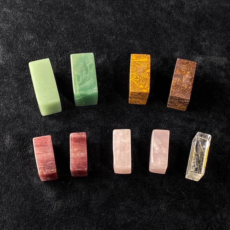 Pu&ograve; includere: Un assortimento di pietre preziose rettangolari in vari colori, tra cui verde, giallo, marrone, rosa e trasparente. Le pietre sono disposte su una superficie scura, mostrando le loro trame e tonalit&agrave; uniche. Per la creazione di gioielli o elementi decorativi.
