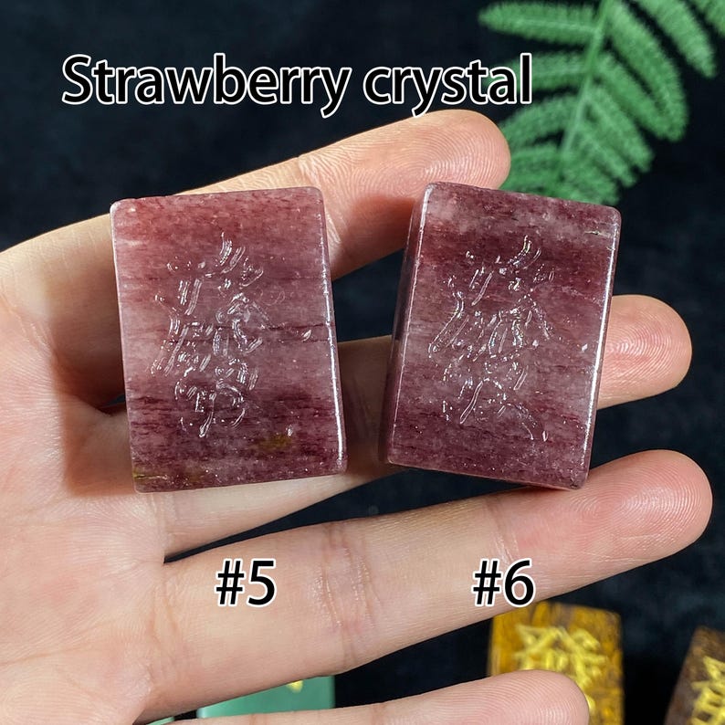Pu&ograve; includere: Due cristalli di fragola rettangolari, numerati #5 e #6, sono tenuti in una mano. I cristalli sono di un colore rosso intenso con motivi intricati. Il testo "Strawberry crystal" &egrave; nella parte superiore dell'immagine.