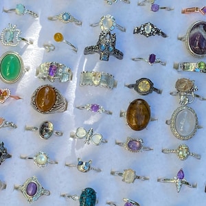 Peut inclure: Une collection de bagues en métal assorties avec diverses pierres précieuses, incluant des cabochons ovales, ronds et en forme de poire dans des tons vert, marron, violet et bleu, ainsi que des formes décoratives comme papillons, crânes et chats.