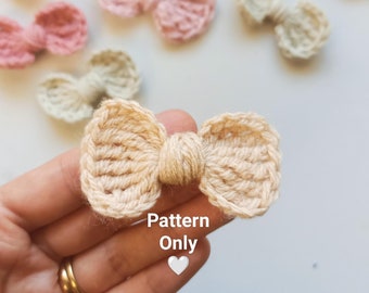 Puede incluir: Una colección de lazos de ganchillo en varios tonos de rosa y beige. Los lazos son pequeños y delicados, perfectos para agregar un toque de encanto hecho a mano a cualquier proyecto. "Pattern Only" está escrito en la imagen.