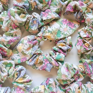 Peut inclure: Un ensemble de chouchous à imprimé floral coloré avec un motif de marguerite. Les chouchous sont faits d'un tissu doux et sont parfaits pour maintenir les cheveux en place.