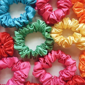 May include: Assortment of colorful satin scrunchies in various shades of pink, blue, green, yellow, and red. The scrunchies are made of soft, silky fabric and are perfect for holding hair in place.