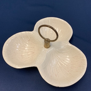 May include: A white ceramic serving dish with three sections and a gold metal handle. The dish has a speckled finish and a scalloped edge.