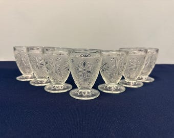May include: Set of eight clear glass cups with a delicate floral pattern. The cups have a footed base and are perfect for serving drinks.