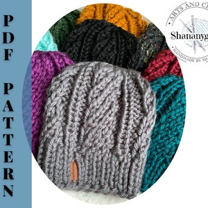 May include: A collection of knitted hats in various colors, including gray, purple, teal, red, black, and yellow. The hats are arranged in a circle, with the gray hat in the center. The hats are all made with a cable knit stitch. The image also includes a logo for "Arts and Crafts Shananygans Handmade by Shannyn".